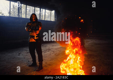 Man portraying warrior Scorpion with chains in his hands poses at the fire and smoke background. Stock Photo