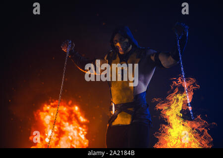 Man portraying warrior Scorpion with chains in his hands poses at the fire and smoke background. Stock Photo