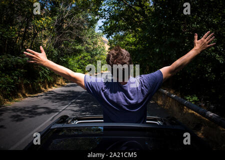 Young happy man drives a car and holds his hand out from the window. Driver enjoys driving and shows Ok sign with his hand out of window. Road trip, t Stock Photo