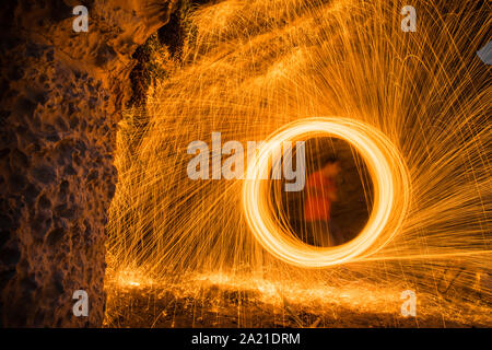 A man doing circular spinning light painting using steel wool at night on the beach. Stock Photo