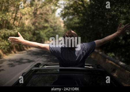 Young happy man drives a car and holds his hand out from the window. Driver enjoys driving and shows Ok sign with his hand out of window. Road trip, t Stock Photo