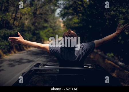 Young happy man drives a car and holds his hand out from the window. Driver enjoys driving and shows Ok sign with his hand out of window. Road trip, t Stock Photo