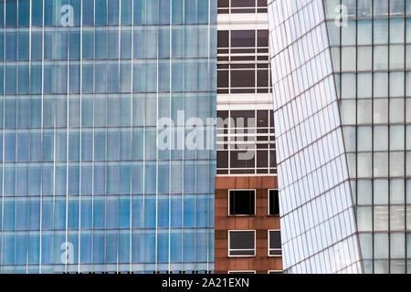 Close up of building facades showing contrast patterns as a different building reveals its face between a curtain of glass facades. Stock Photo