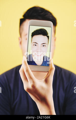 Smiling handsome Vietnamese man taking selfie on smartphone in his hand Stock Photo