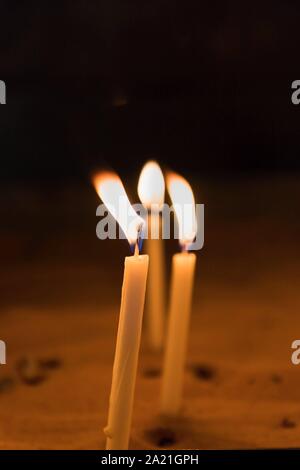 Three yellow candles burning in the dark, copy space Stock Photo