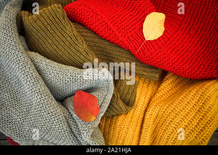 A pile of different-colored knitted things and autumn leaves. Stock Photo