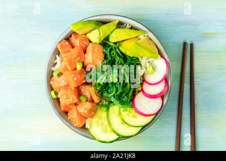 Salmon poke with avocado, wakame and cucumber, shot from the top on a teal blue background with chopsticks Stock Photo