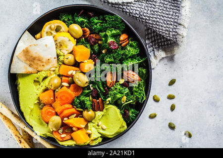 Avocado hummus with baked vegetables, olives, nuts and berries in a black plate. Healthy vegan food concept. Stock Photo