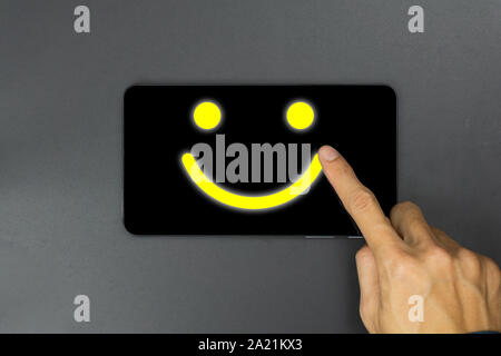 Conceptual the customer responded to the survey. The client using hand write happy face smile icon on tablet. Depicts that customer is very satisfied. Stock Photo