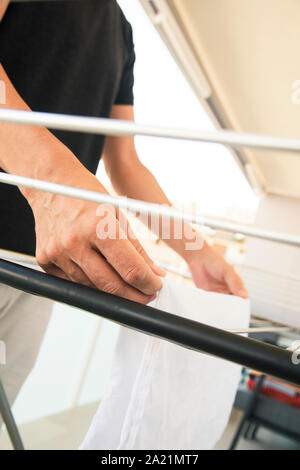 closeup of a young caucasian man hanging wet clothes on a drying rack in a balcony Stock Photo