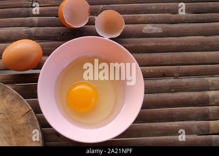 shell with egg and open Eggs in a pink bowl Placed near to the butcher on Bamboo battens.Top view closeup. Stock Photo