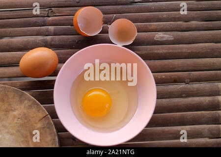 shell with egg and open Eggs in a pink bowl Placed near to the butcher on Bamboo battens.Top view closeup. Stock Photo