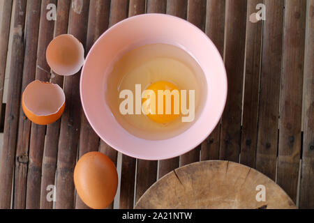 shell with egg and open Eggs in a pink bowl Placed near to the butcher on Bamboo battens.Top view closeup. Stock Photo