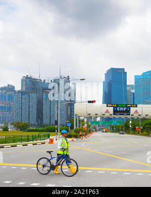 SINGAPORE - FEBTUARY 16, 2017: Construction site worker in helmet and vest crossing road with bicycle, Singapore downtown skyline in background Stock Photo