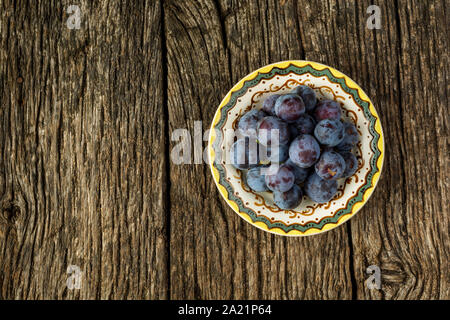 Flat lay. Ripe plums on old vintage plate on dark rustic wooden background Stock Photo