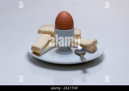 Boiled chicken's egg, in an egg cup with buttered bread, soldiers, and a tea spoon on a white plate Stock Photo