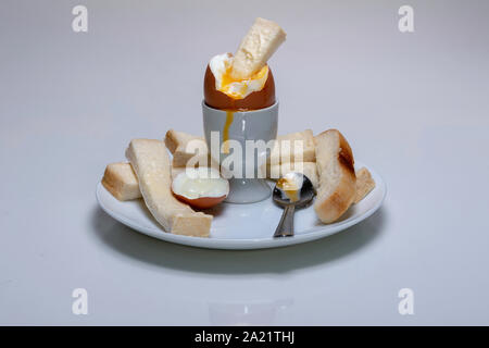soft boiled chicken's egg, in an egg cup with buttered bread, soldiers, and a tea spoon resting on a plate Stock Photo