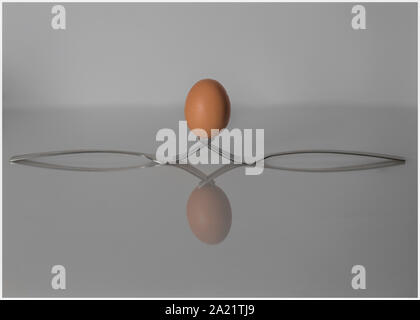 Chicken's egg balanced on two forks, with a reflection. Stock Photo