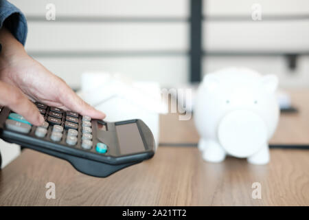 hand calculating with calculator. house model piggy bank on office desk. saving money for buying house property. real estate investment finance & bank Stock Photo