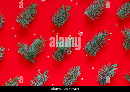 Festive pattern made of blue Christmas tree branches and silver star shaped confetti on a red background. Stock Photo