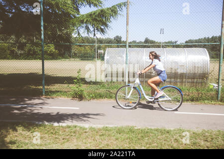 Portrait of happy attractive young woman in jeans shorts with bicycle in the park on summer day. Stock Photo