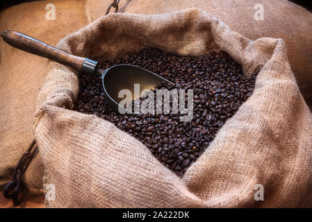 Roasted black coffee beans and an old scoop, in a jute sack. Vintage image of coffee beans in jute packaging. Open jute bag with coffee beans. Stock Photo