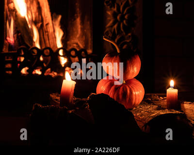 Two halloween pumpkins standing in the dark on birch logs surrounded by burning candles. In the background is a flame from a fireplace. Stock Photo