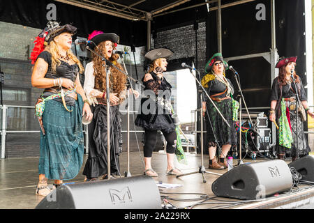 Pirate Day in Hastings. Female Harmony group, The Rattlebag Singers on sound stage in full pirate costume, standing in line singing into microphones. Stock Photo