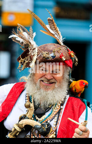 Pirate Day in Hastings. Close up head and shoulder of senior man dressed as Long John Silver with brushy grey beard, parrot on shoulder, smiling. Stock Photo