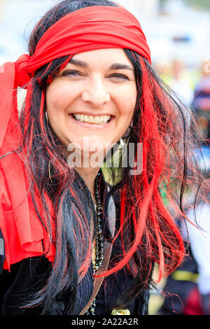 Pirate Day in Hastings, UK. Close up of pretty Caucasian young woman, dressed up as pirate and smiling at viewer. Black and red hair. Stock Photo