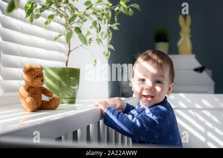 Happy kid near window on white bed in his room Stock Photo