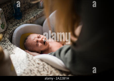 Crying newborn getting a bath in the sink for the first time at home