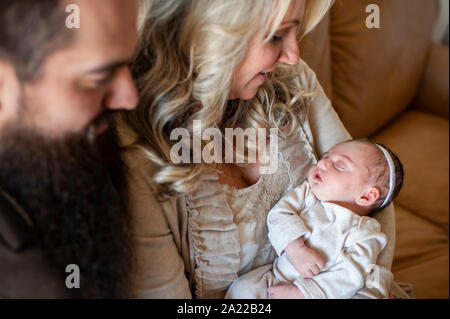 Mother and father looking at their newborn baby girl on couch at home Stock Photo