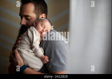 Father embracing sleeping newborn daughter on shoulder at home Stock Photo