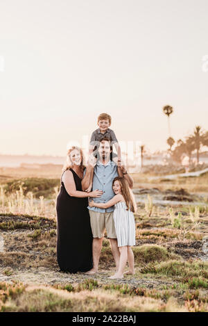 Portrait of happy smiling family of four hugging on beach at sunset Stock Photo