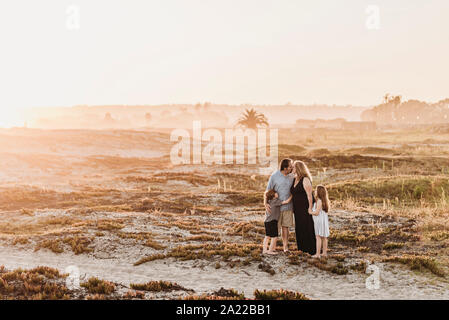 Side view of happy family of four on beach at sunset Stock Photo