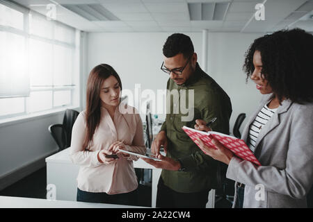 Group of diverse business team are using a digital tablet discussing online projects and writing notes in diary Stock Photo