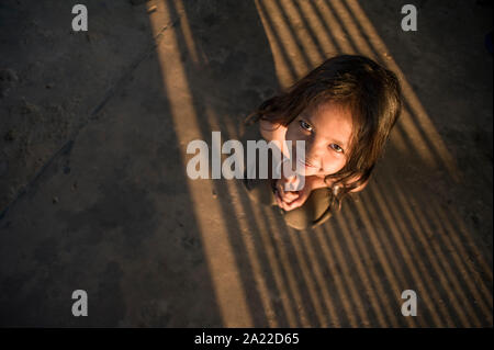 Sweet litlle Cambodian girl crouching on shaded ground Stock Photo
