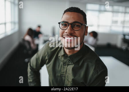 Portrait of charming successful young african american entrepreneur in shirt and eyeglasses looking at camera with smile in office Stock Photo