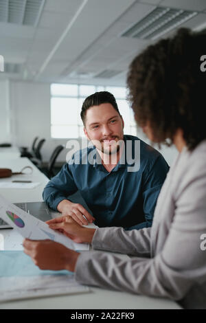 Smiling young businessman sitting with his female colleague at the table analyzing financial reports in office Stock Photo