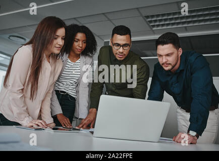 Group of concentrated diverse business team discussing information on laptop screen over the desk in office Stock Photo