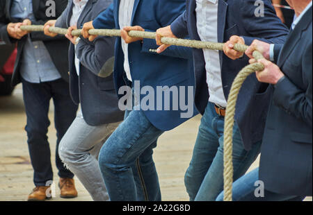 Men with business clothing and formal jackets pulling together on a thick rope, concept photo of the expression "pulling together". Stock Photo