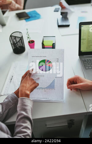 Close-up of businesswoman analyzing finance graph paper with her colleague on office desk Stock Photo