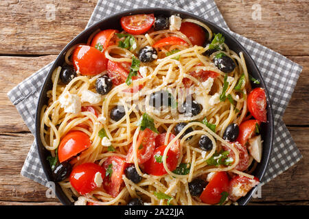 Traditional Greek pasta spaghetti salad with cheese, olives, tomatoes close-up on a plate on the table. Horizontal top view from above Stock Photo