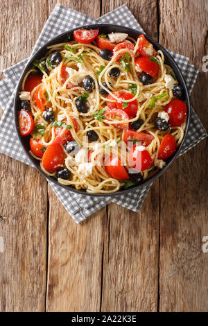 Tasty greek pasta salad with cheese, olives, tomatoes and parsley close-up on a plate on the table. Vertical top view from above Stock Photo