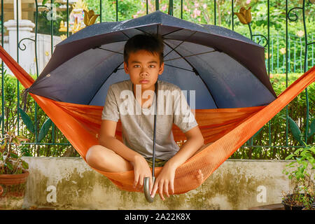 Children under the umbrella on the hammock when it rains. Stock Photo