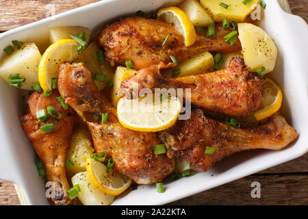 Tasty chicken legs baked with lemon and boiled potatoes in garlic sauce close-up in a baking dish on the table. Horizontal top view from above Stock Photo
