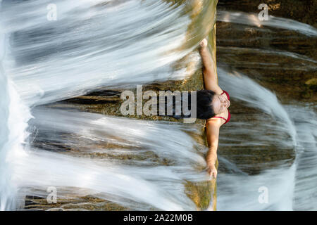 Woman outstretching her arms inside the powerful waterfall flow, Thailand Stock Photo