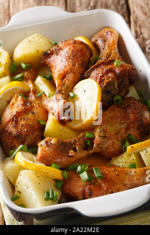 Baked chicken legs with lemon and boiled potatoes close-up in a baking dish on the table. vertical Stock Photo