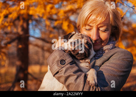 Woman walking pug dog in autumn park. Happy lady hugging pet. Best friends Stock Photo